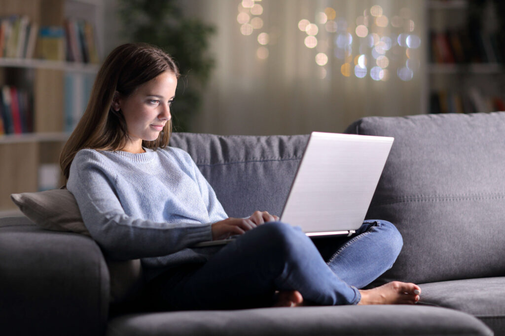 woman in blue sweater and jeans sits on couch using computer